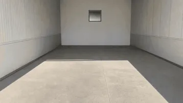 Leerer, sauberer Raum mit Betonboden und einer kleinen Fensteröffnung, gut beleuchtet.