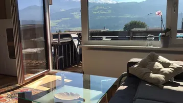 Helles Wohnzimmer mit Zugang zum Balkon und beeindruckendem Bergblick durch große Fenster.