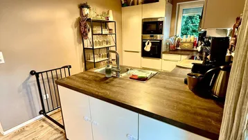 Moderne Küche mit Holzarbeitsplatte, integrierter Spüle und Einbaugeräten. Der Boden ist mit Holzplanken ausgelegt.