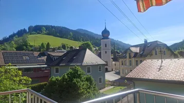 Balkon mit Blick auf ein Dorf mit Kirche und umliegende grüne Hügellandschaft.