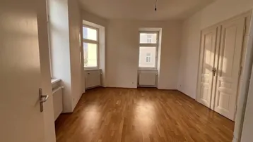 Helles, leeres Zimmer mit Parkettboden und zwei Fenstern, bereit zur individuellen Gestaltung.