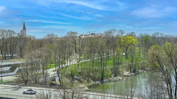 Weitläufiger Blick auf einen Fluss, grüne Bäume und eine Stadtlandschaft unter blauem Himmel.