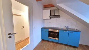 Funktionale Küchenzeile mit blauen Unterschränken, Herd und Spüle im Dachgeschoss.