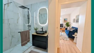 Modernes Badezimmer mit begehbarer Dusche, schwebendem Waschtisch und Blick in ein helles Wohnzimmer.