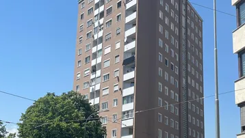 Hohes Wohngebäude mit vielen Etagen und Balkonen an einer belebten Straße in der Stadt.
