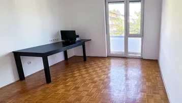 Helles Zimmer mit Parkettboden, Schreibtisch und Zugang zu einem französischen Balkon.