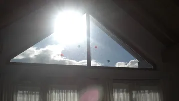Helles Giebelfenster im Dachgeschoss, das viel Sonnenlicht und einen weiten Blick auf den bewölkten Himmel bietet.