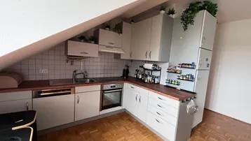 Funktionale Küche in Dachgeschosswohnung mit hellgrauen Schränken, Holzarbeitsplatte und Parkettboden.