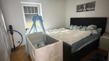 Helles Schlafzimmer mit Doppelbett, Babybett und Holzfußboden, ideal für Familien.