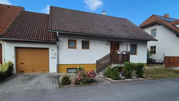 Einfamilienhaus mit Garage, Vorgarten und gepflasterter Zufahrt unter blauem Himmel.