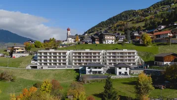 Neubau-Wohngebäude in alpiner Landschaft mit Blick auf ein Dorf und Berge.