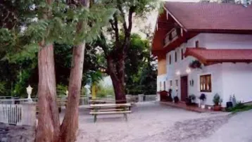 Traditionelles Landhaus mit rotem Ziegeldach, umgeben von hohen Bäumen und einem gepflegten Außenbereich.