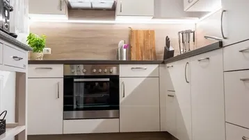 Moderne Küche mit weißen Schränken, Dunstabzugshaube und integriertem Backofen.