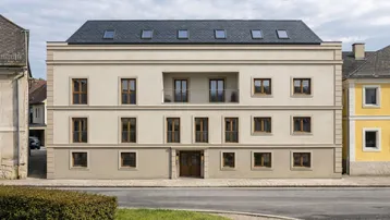 Modernes Wohngebäude mit heller Fassade, Mansarddach und kleinen Balkonen.