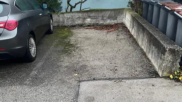 Außenparkplatz mit Betonmauern und angrenzendem Gebäude, umgeben von Bäumen und Sträuchern.