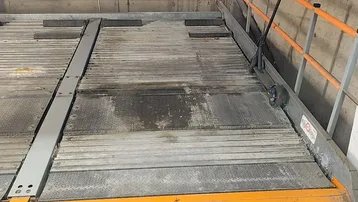 Funktionales mechanisches Parksystem in einer Tiefgarage mit robusten Betonwänden und auffälligen orangefarbenen Sicherheitsgeländern.