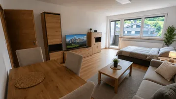 Helles, offenes Wohn- und Schlafzimmer mit Essbereich, Holzboden und Bergblick vom Balkon.