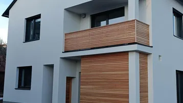 Modernes Einfamilienhaus mit weißer Fassade, Holzverkleidung und Balkon unter klarem Himmel.