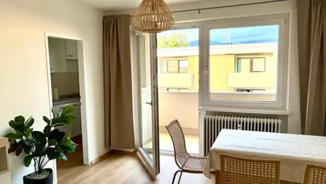 Heller Wohn-Essbereich mit Holzboden, Zugang zum Balkon und moderner Hängelampe.