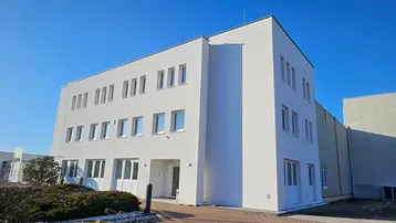 Modernes dreistöckiges Bürogebäude mit weißer Fassade und vielen Fenstern unter blauem Himmel.