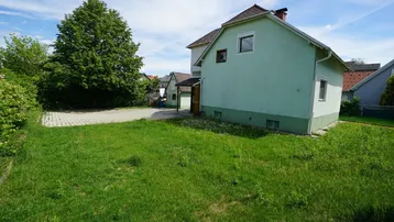 Großer Gartenbereich neben dem Haus mit Rasenfläche und weiteren Gebäuden im Hintergrund.