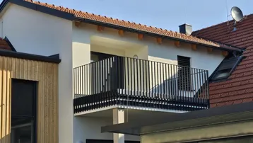 Moderner Balkon mit schwarzem Geländer an einem Wohngebäude mit Holzverkleidung.