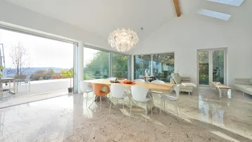 Heller, offener Wohn-Essbereich mit hohen Decken, Marmorboden und Zugang zur Terrasse mit Weitblick.