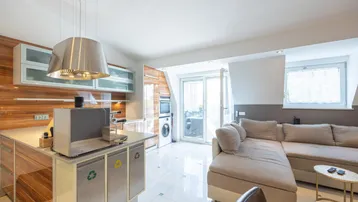 Moderne Wohnküche mit integriertem Wohnbereich, hellen Fliesen und Zugang zum Balkon.