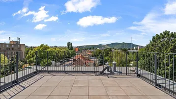 Große Dachterrasse mit Fliesenboden und weitem Blick über die Stadt und grüne Hügel.