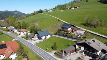 Weitläufige Luftaufnahme der ländlichen Umgebung mit Wohnhäusern, Straße und grünen Hügeln.