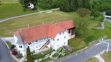 Luftaufnahme eines Gebäudekomplexes mit rotem Ziegeldach und umliegender grüner Landschaft.