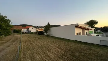 Ländliche Umgebung mit Feldern, Häusern und sanften Hügeln im Hintergrund bei Sonnenuntergang.