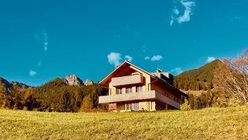 Modernes Holzhaus in alpiner Landschaft mit weitem Blick auf die Berge und grüne Wiesen.
