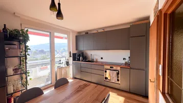 Moderne Küche mit grauen Schränken, Holzarbeitsplatte und Zugang zum Balkon.