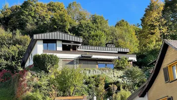 Haus auf einem bewaldeten Hügel mit moderner Architektur und viel Grün.