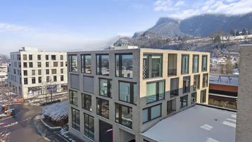 Modernes Bürogebäude mit großen Fenstern und Blick auf schneebedeckte Berge und die Umgebung.
