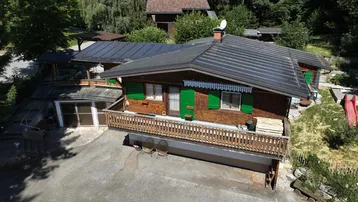 Luftaufnahme des Holzhauses mit Solarpaneelen auf dem Dach und umgebender Natur.