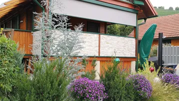 Charmantes Holzhaus mit Balkon, gepflegtem Vorgarten und dekorativen Pflanzen.