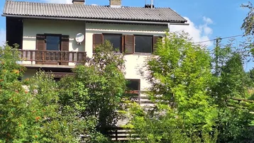 Traditionelles Haus mit Balkon und grüner Umgebung unter blauem Himmel.