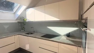 Moderne Küche mit hellen Schränken, Granitarbeitsplatte und Dachfenster, durchflutet von Sonnenlicht.