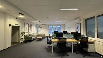 Modern eingerichtetes Großraumbüro mit mehreren Arbeitsplätzen und einem gemütlichen Lounge-Bereich.