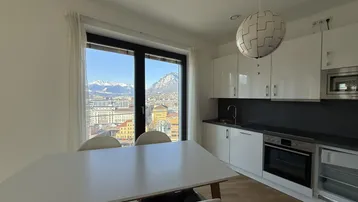 Moderne Küche mit Essbereich, weißen Hochglanzfronten und beeindruckendem Bergblick.