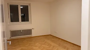 Helles Zimmer mit Fischgrätparkettboden und Fenster, ideal als Schlaf- oder Arbeitszimmer.