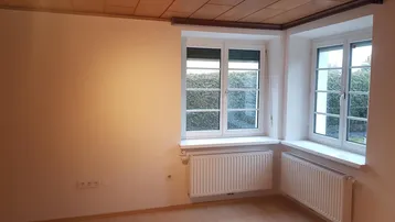 Helles Zimmer mit Laminatboden, Holzdecke und zwei Fenstern mit Blick ins Grüne.