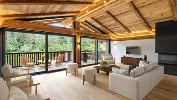 Geräumiges Wohnzimmer im alpinen Stil mit Holzbalkendecke, Kamin und Zugang zum Balkon mit Waldblick.