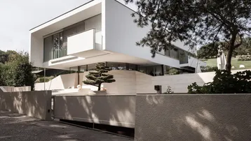 Moderne, weiße Villa mit klaren Linien und großen Glasflächen, umgeben von einer gepflegten Grünanlage.
