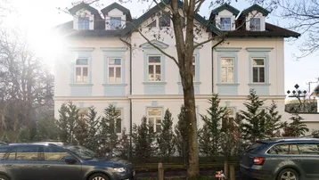 Klassische Fassade einer eleganten Stadtvilla mit hellen Wänden, grünen Dächern und dekorativen Elementen, beleuchtet von der Wintersonne.