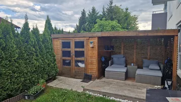 Gemütlicher Gartenbereich mit Holzschuppen und überdachtem Sitzbereich, umgeben von hohen Hecken.