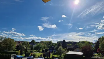 Sonniger Ausblick auf eine grüne Wohngegend mit blauem Himmel und vereinzelten Wolken.