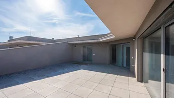 Große, sonnige Terrasse mit modernen Fliesen und Zugang zu den Innenräumen.